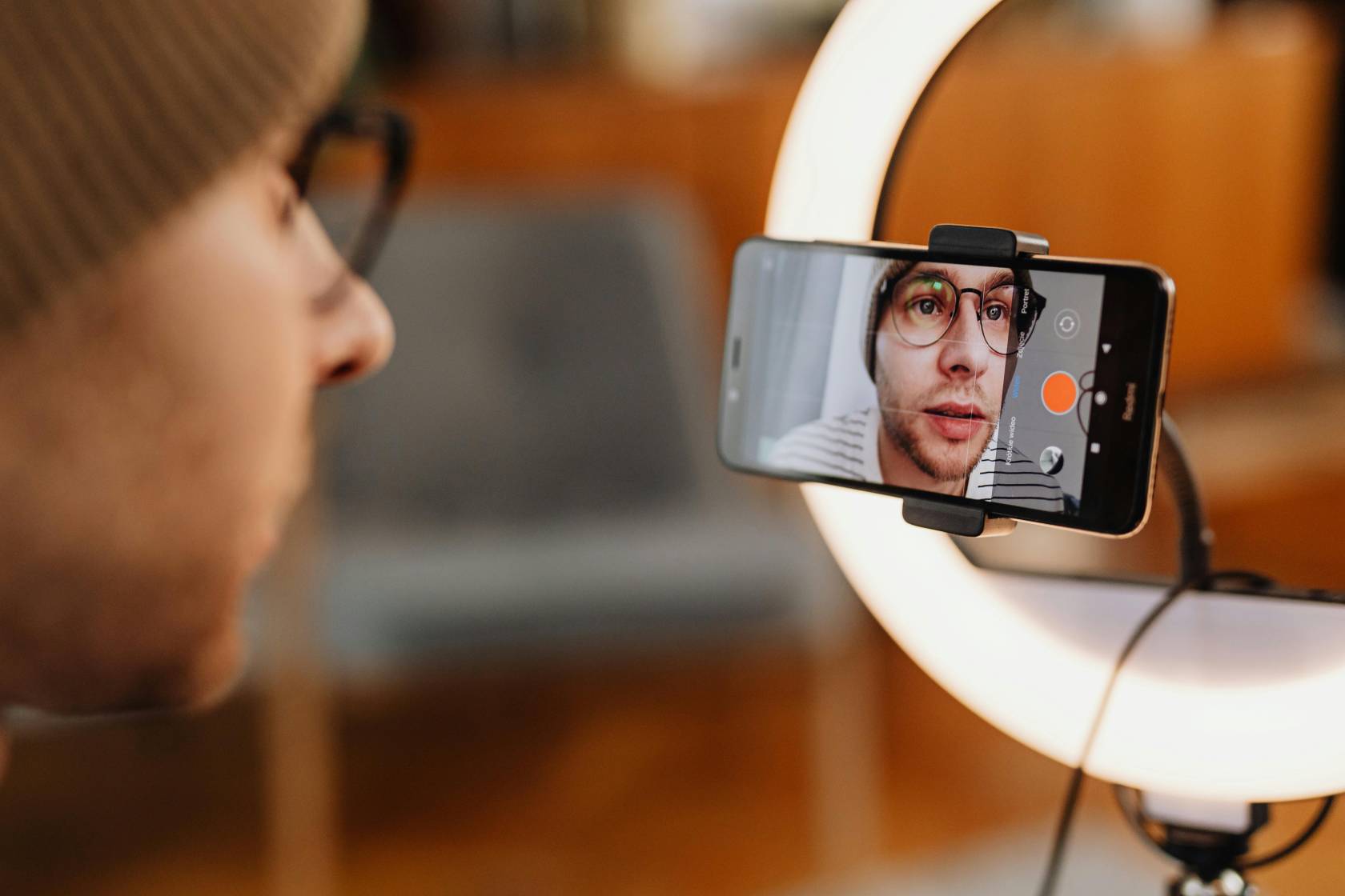 Person wearing hat and glasses holding a mobile phone in front of a camera, discussing going live on TikTok.